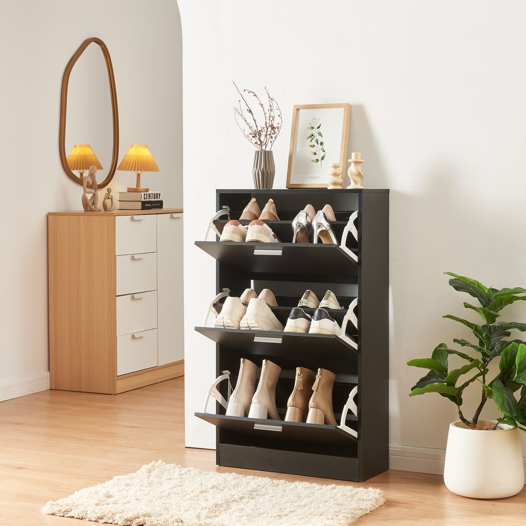 A shoe cabinet with multiple shelves and flip-down doors, filled with various shoes, is shown in a room with a mirror and a plant.