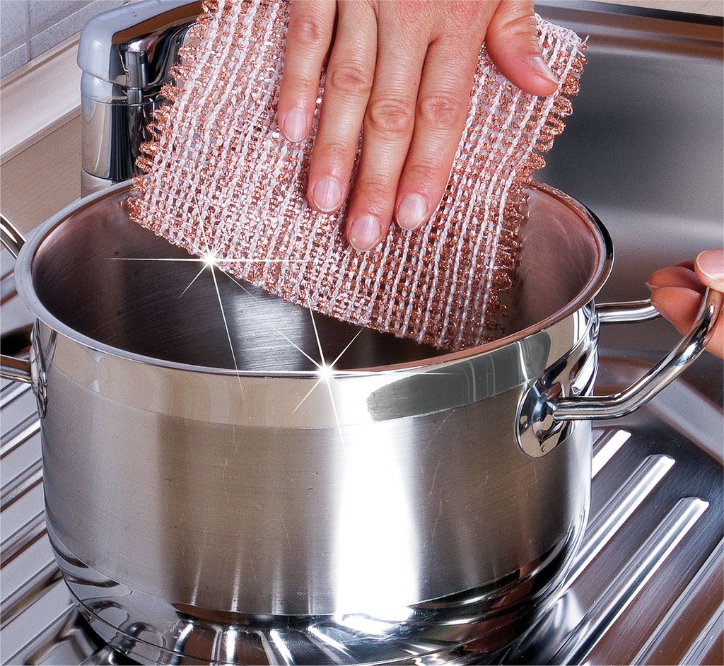 A hand is shown scrubbing the inside of a stainless steel pot with a copper-colored scrubber.