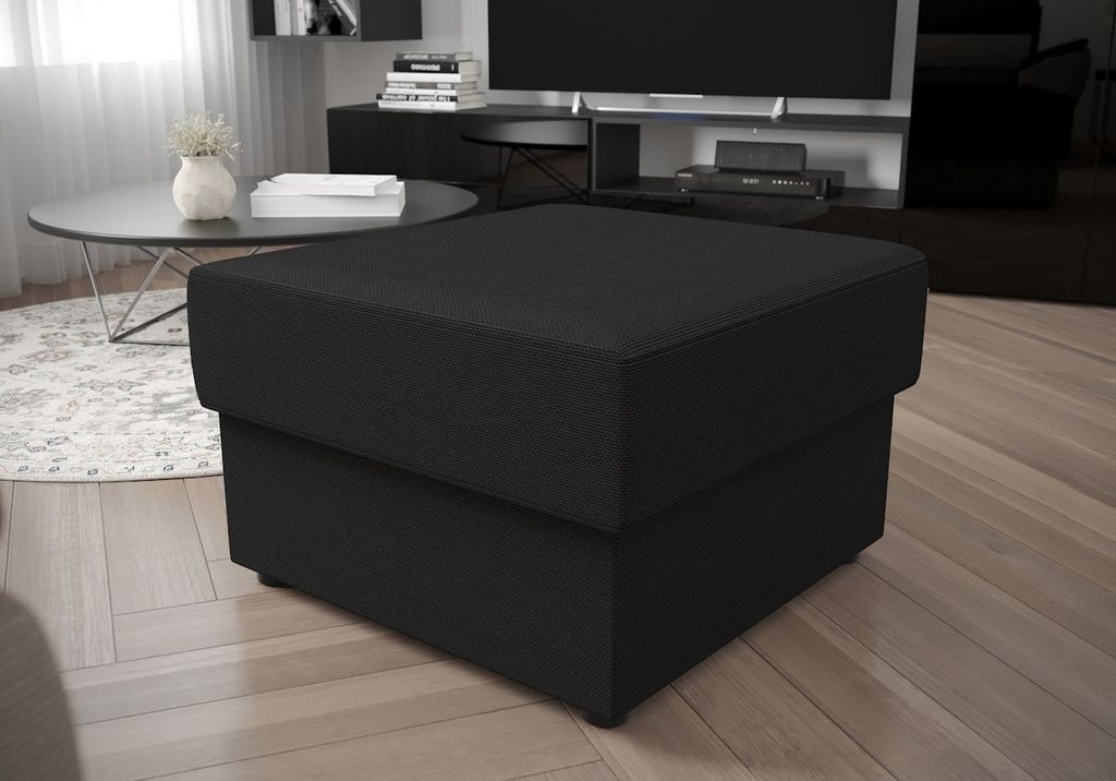 A dark gray ottoman is placed in a modern living room setting, with a coffee table and a television in the background.