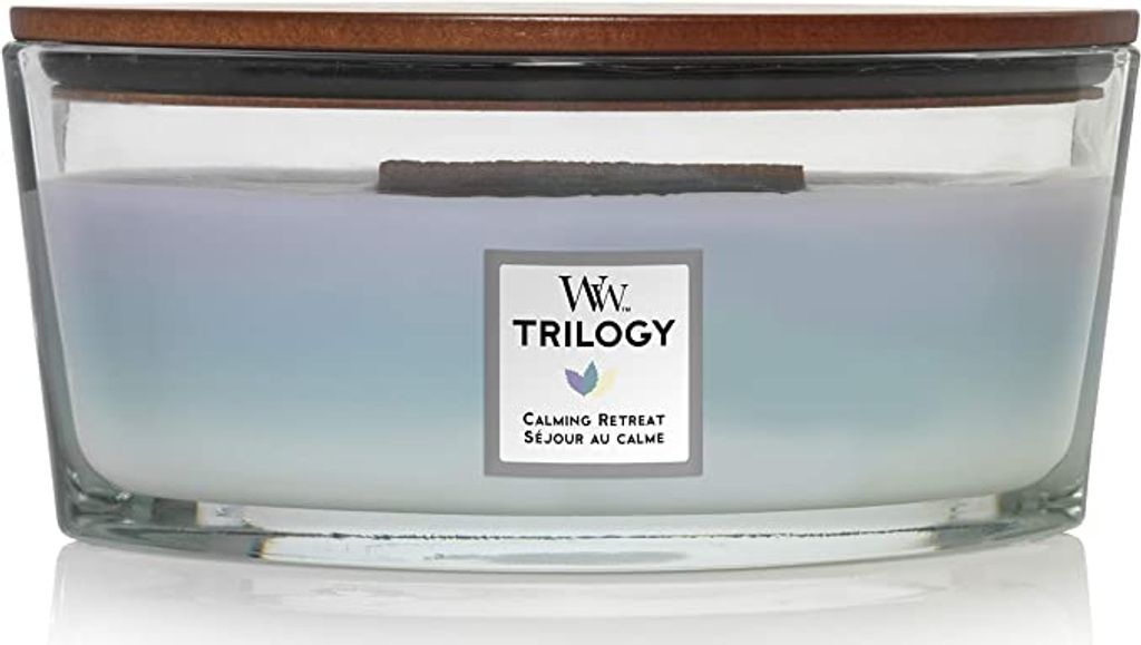 A large, multi-layered candle in a clear glass container with a wooden lid.
