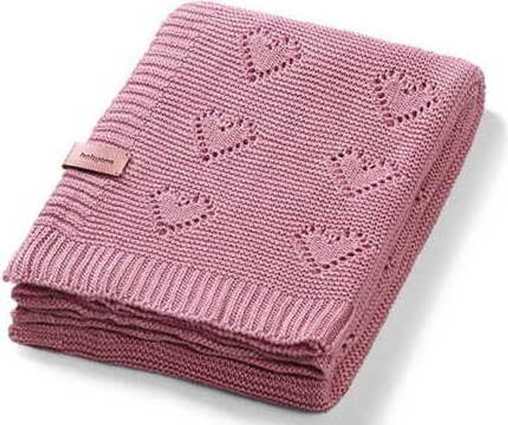 A folded pink knitted baby blanket with a heart pattern and a small tag.