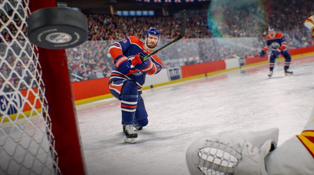 A hockey player in a blue and orange uniform is skating on an ice rink, about to hit a puck that is flying towards the camera. The background shows a stadium filled with spectators.