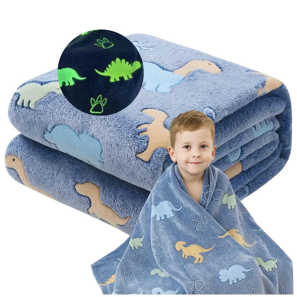 A young boy is wrapped in a blue blanket with dinosaur patterns. The blanket is folded in the background.