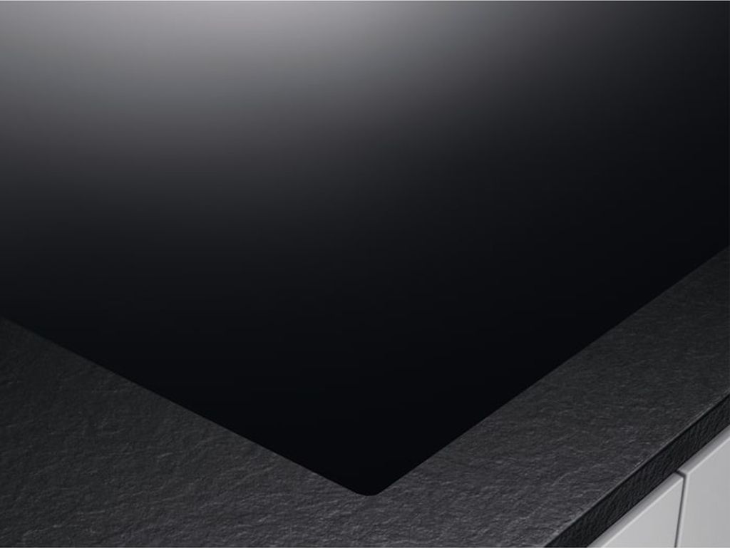 A close-up view of a black glass ceramic hob with a textured gray edge.