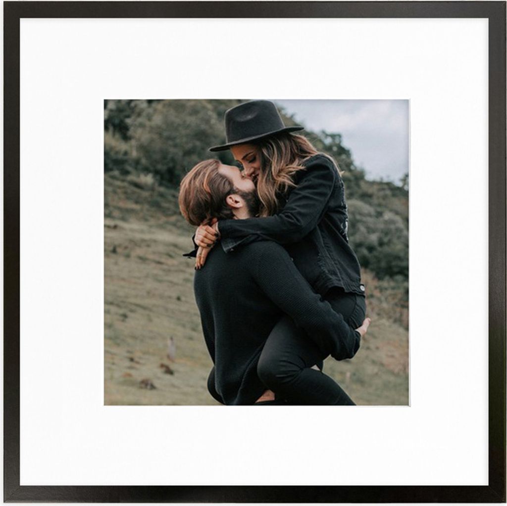 A couple kissing outdoors, with the man holding the woman. The image is framed.