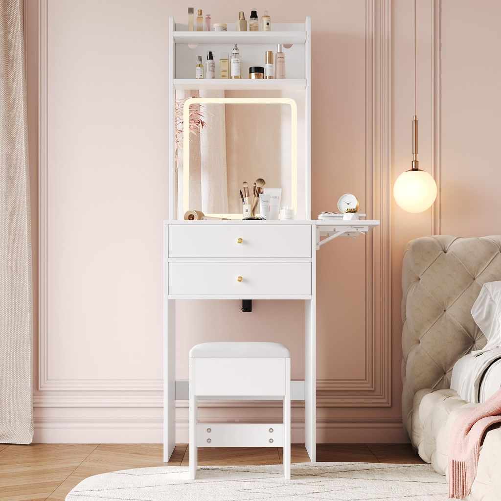 A white vanity table with a lighted mirror and stool is set up in a bedroom with pink walls.
