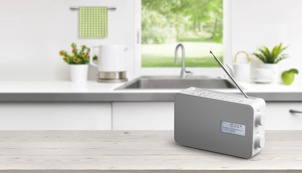 A gray and white Panasonic DAB+ radio sits on a wooden table in a bright, modern kitchen setting.