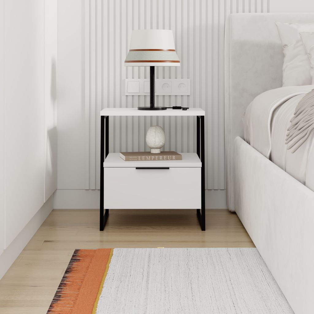 A modern white nightstand with a drawer and shelf, placed next to a bed.