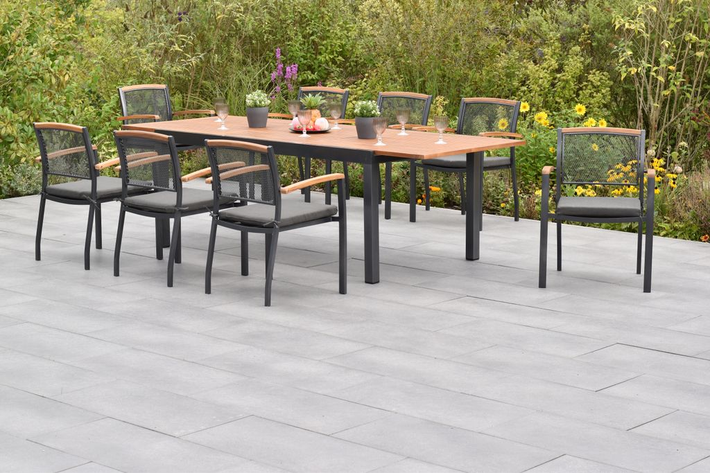 An outdoor dining set with a table and chairs on a patio, surrounded by greenery and flowers.