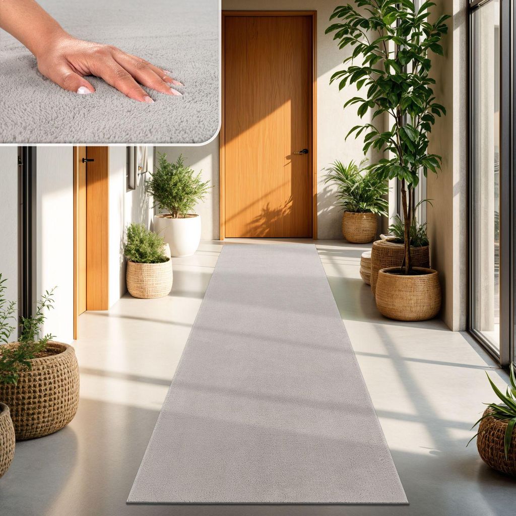 A hand touching a soft gray rug in a hallway with plants and wooden doors.