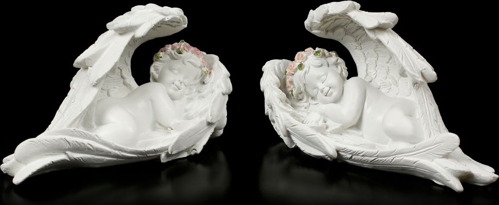 Two white angel figurines with pink floral accents, lying down with wings spread, against a black background.