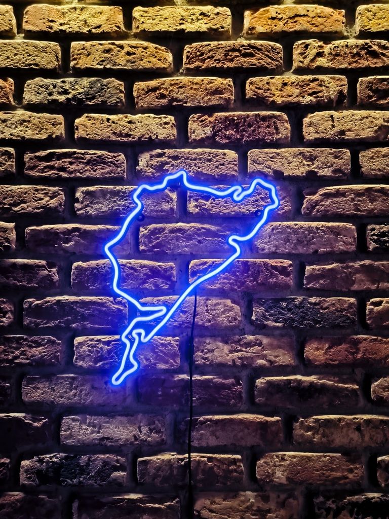 A blue neon outline of the Nurburgring Nordschleife race track is mounted on a brick wall.