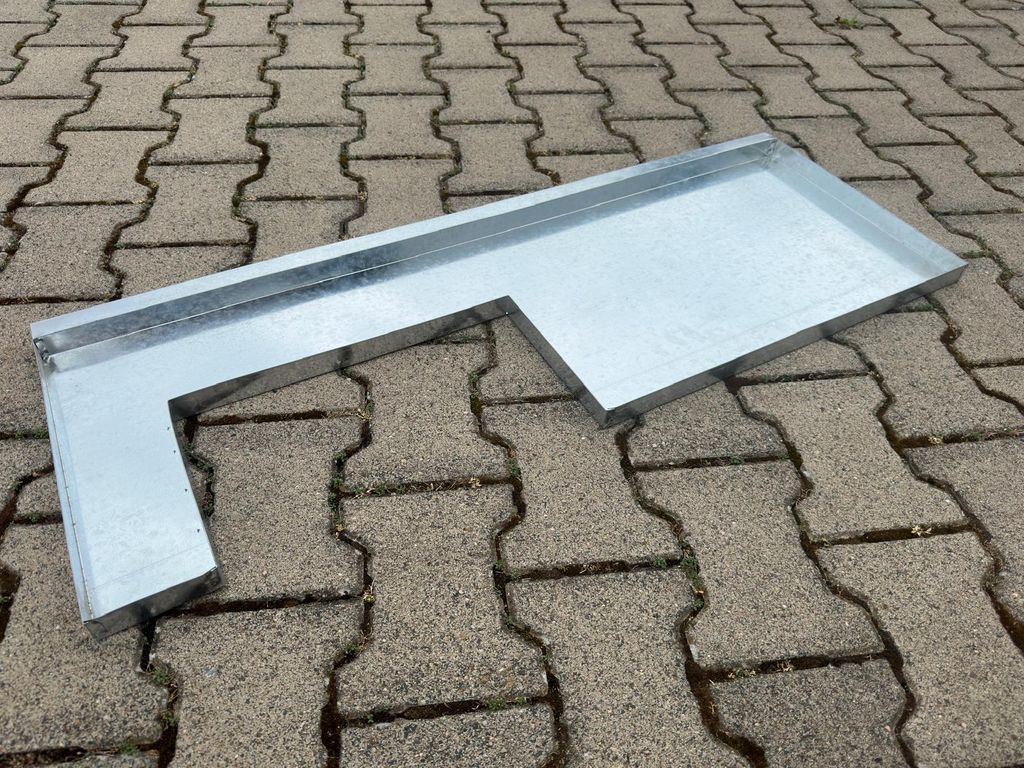 A galvanized metal tray with an L-shape, lying on a paved surface.