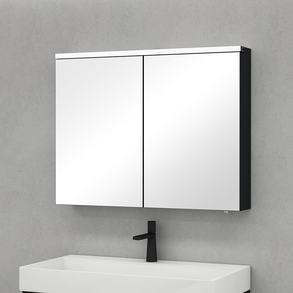 A mirrored medicine cabinet with two doors is mounted on a light gray wall above a white sink with a black faucet.