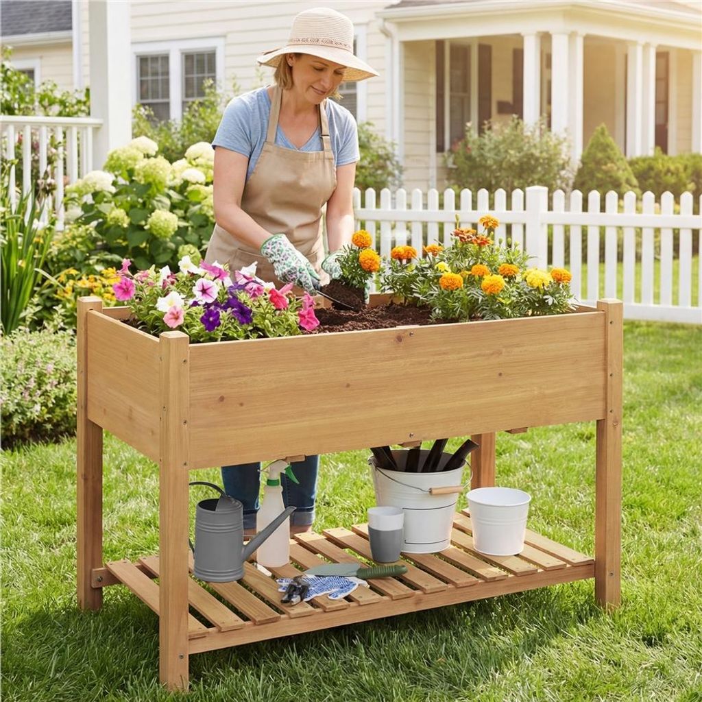 A woman is gardening in a raised planter in a backyard setting.