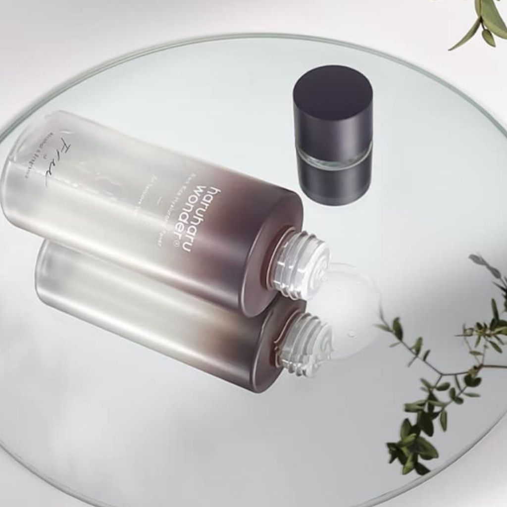 A bottle of toner is shown on a reflective surface with some greenery in the background.