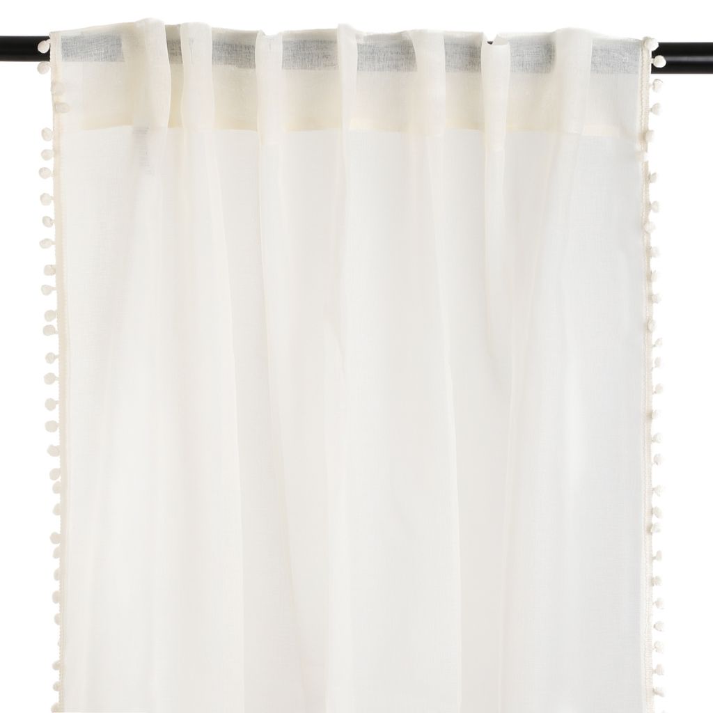 A close-up view of a cream-colored curtain with pom-pom trim hanging from a curtain rod.