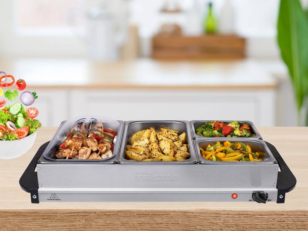 A buffet food warmer with three compartments filled with food, placed on a wooden table in a kitchen setting.