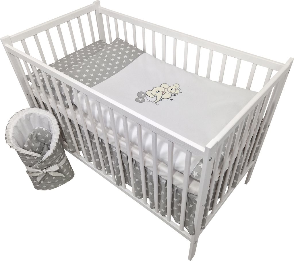 A white wooden crib filled with baby bedding. A grey and white star-patterned blanket is rolled up and tied with a bow to the left of the crib.