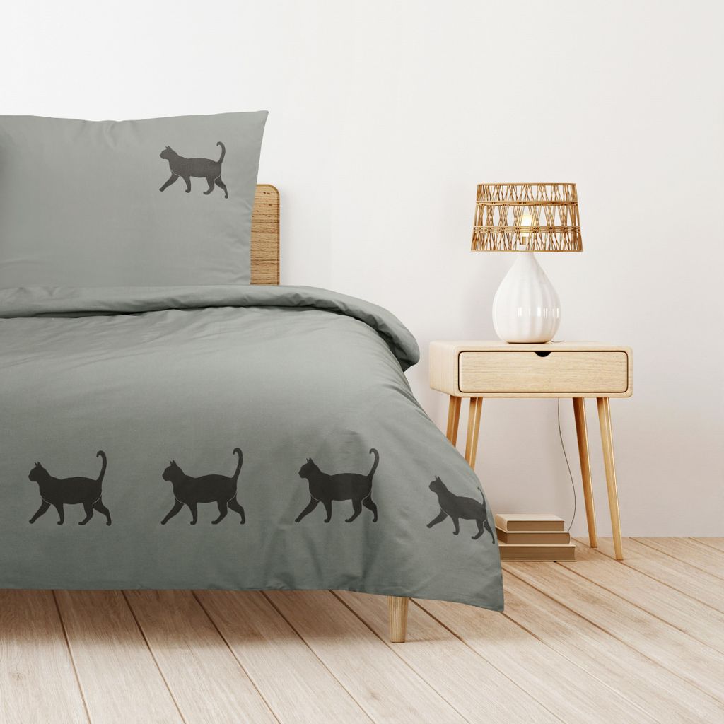 A bed with a duvet cover and pillowcase featuring a cat silhouette pattern, placed in a bedroom setting with a nightstand and lamp.