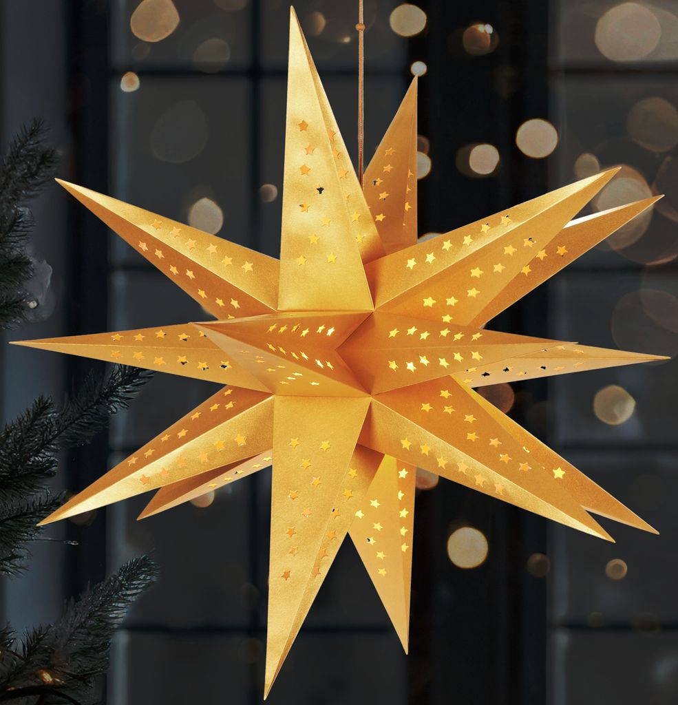 A golden, star-shaped paper lantern with cut-out stars is illuminated from within, hanging in front of a dark background with bokeh lights.