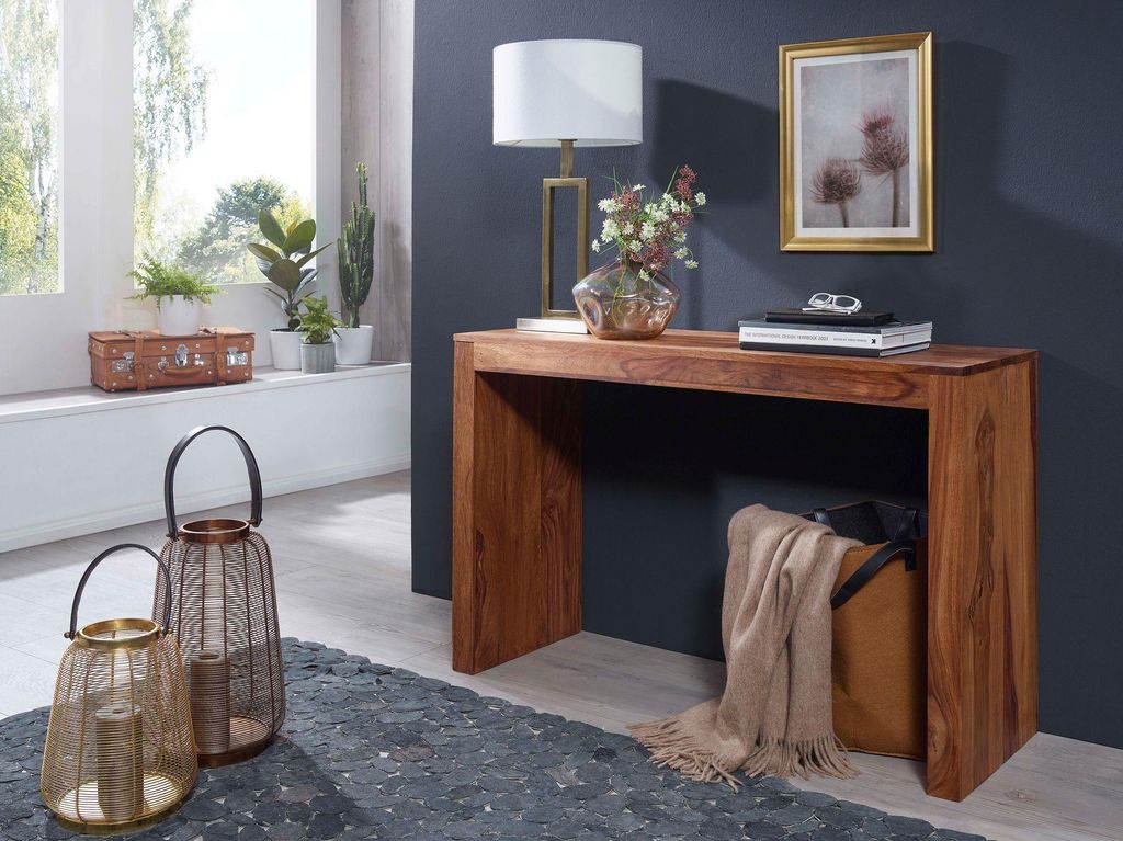 A console table with a lamp, vase, and books on top, placed in a room with a window and decorative lanterns.