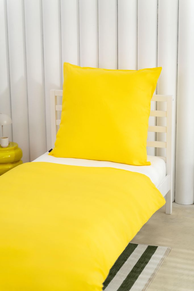 A yellow duvet and pillow set on a white bed frame.