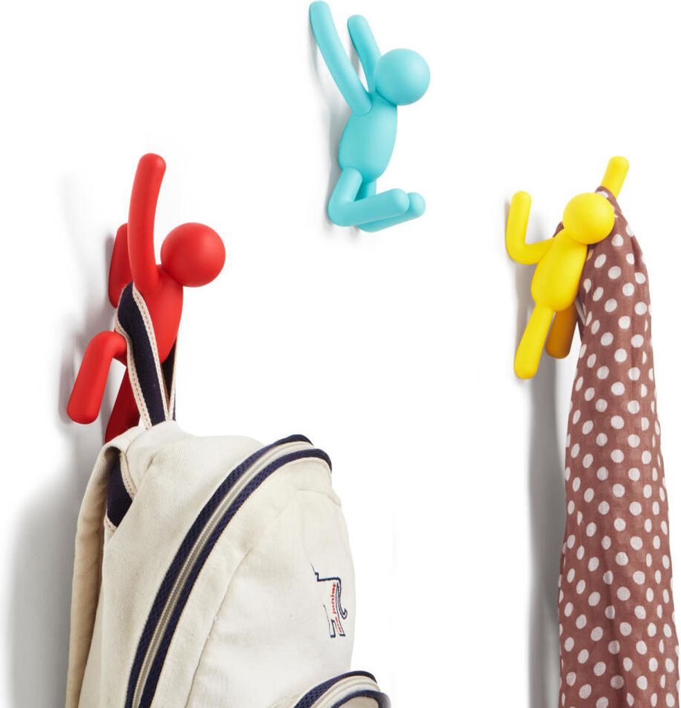 Three colorful, stylized human-shaped hooks mounted on a white wall, with a backpack hanging from one and a scarf from another.