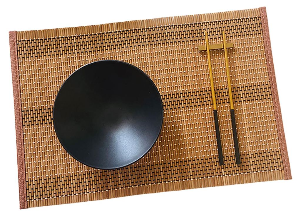 A black bowl and chopsticks are placed on a bamboo placemat.