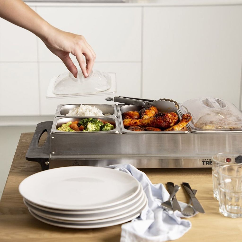 A hand is placing a lid on a buffet food warmer filled with various dishes, including rice, vegetables, and chicken.