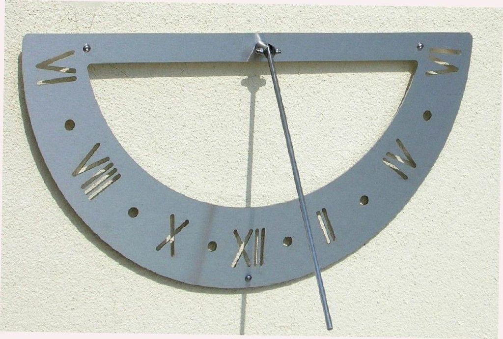 A metal sundial with Roman numerals mounted on a textured wall.