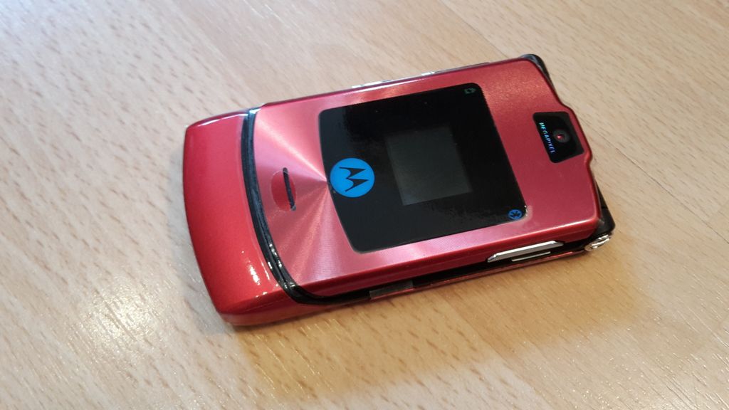 A red Motorola RAZR V3i flip phone is shown on a wooden surface.