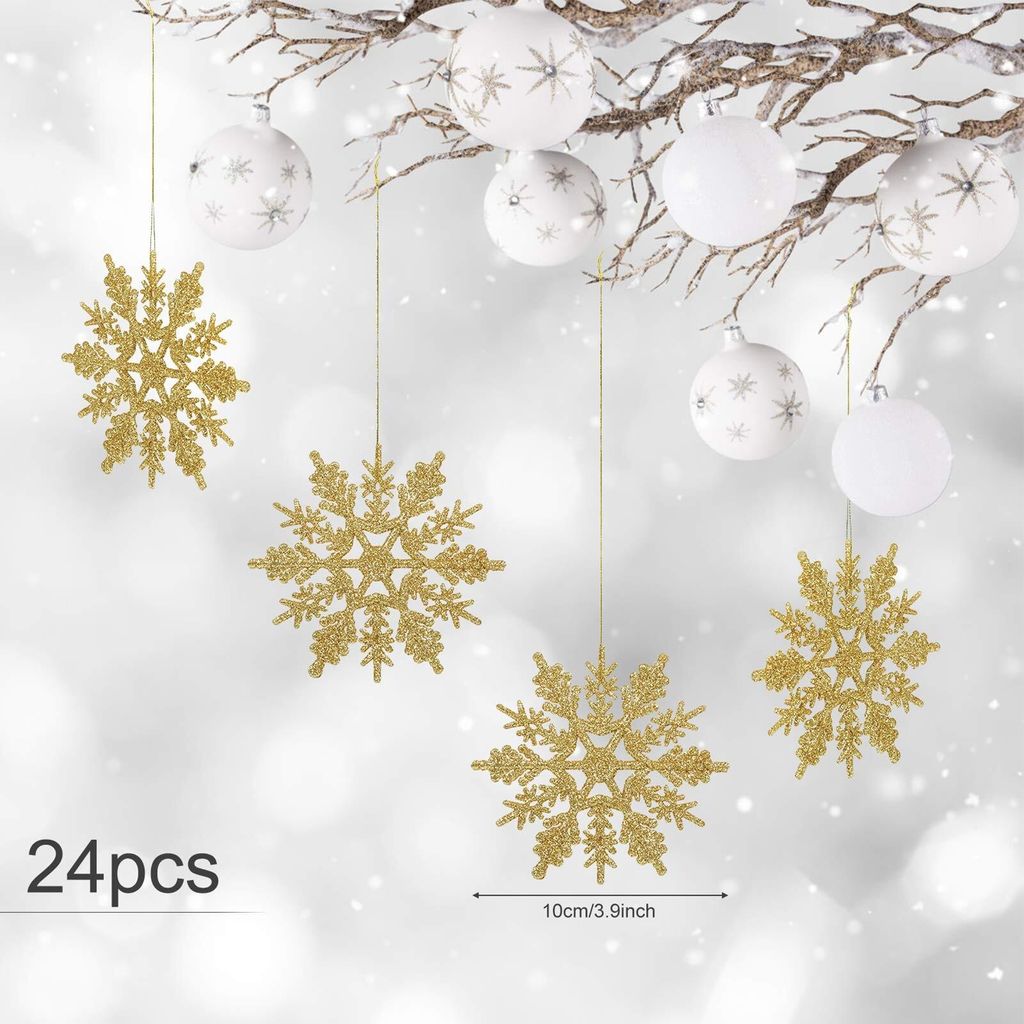 Gold glitter snowflakes and white Christmas ornaments hang from a branch against a blurred snowy background.
