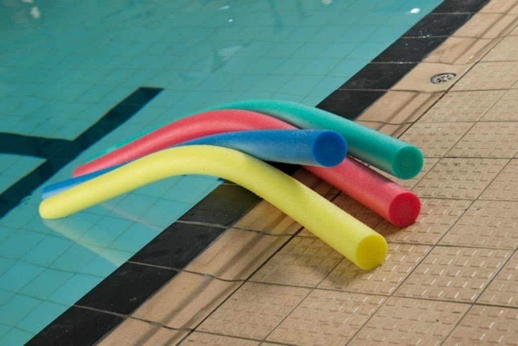 Several colorful swimming noodles are resting on the edge of a swimming pool.