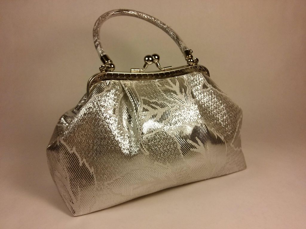A silver handbag with a floral pattern is displayed against a light gray background.