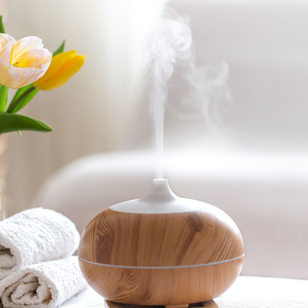 An aroma diffuser with steam rising, next to folded towels and tulips.