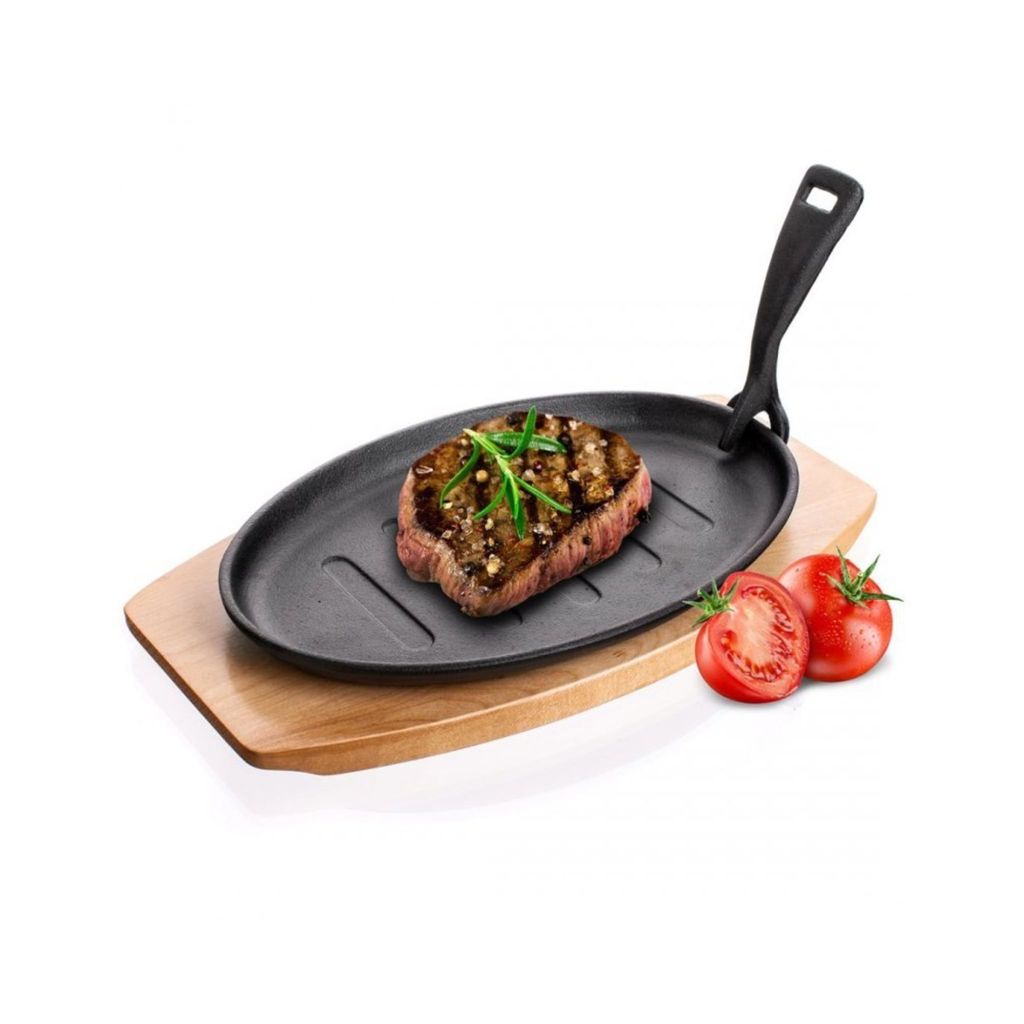 A grilled steak on a cast iron pan, served on a wooden board with tomatoes.