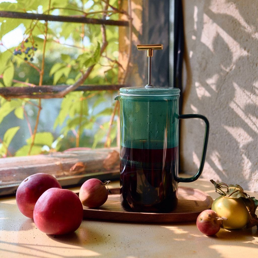 A French press with fruit on a windowsill.