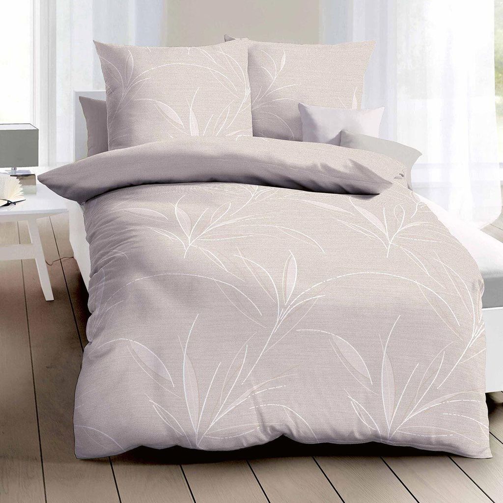 A neatly made bed with beige bedding featuring a white leaf pattern, set against a bright window.