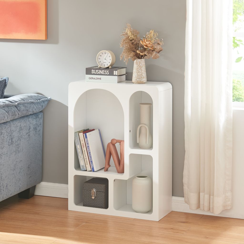 A white shelving unit with decorative items and books, placed next to a sofa and a window with curtains.