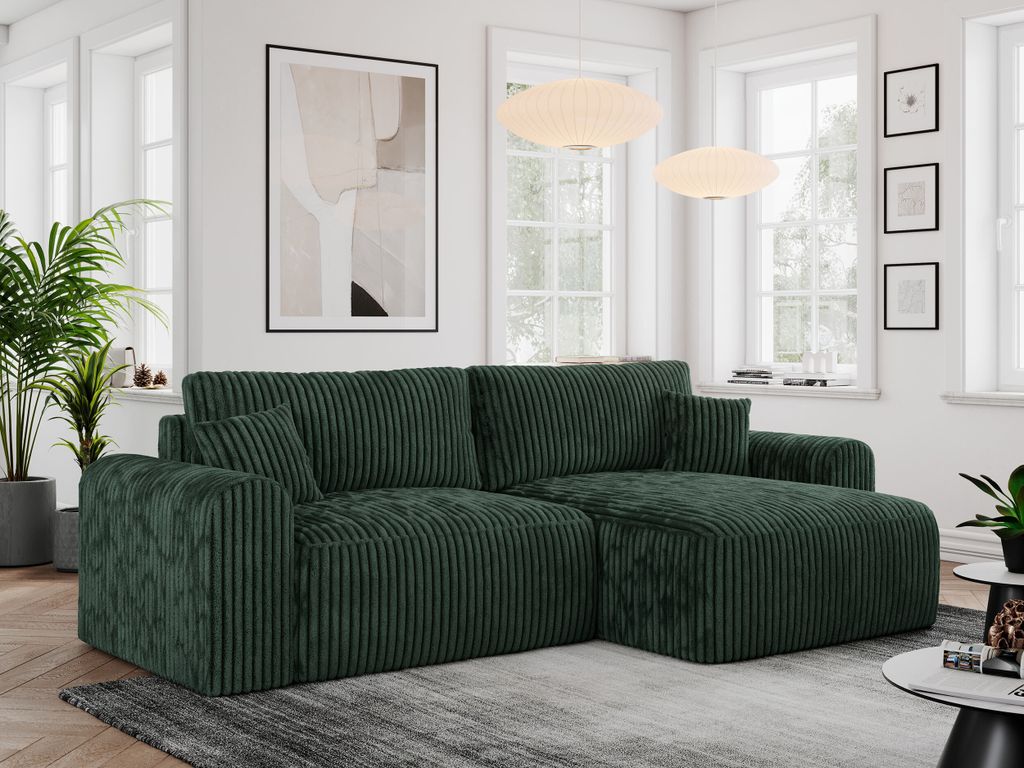 A dark green corduroy sectional sofa is shown in a well-lit living room setting, with large windows in the background.
