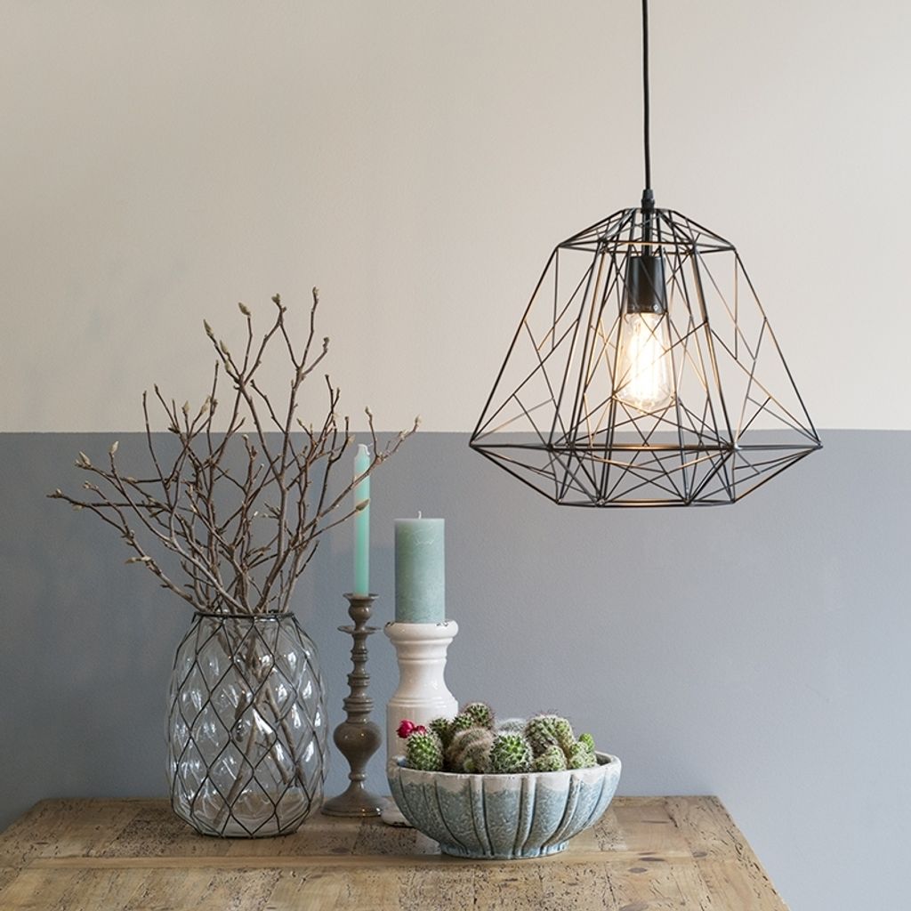 A modern industrial-style pendant lamp is displayed in a home decor setting, alongside decorative items like a vase with branches, candles, and a bowl of cacti.