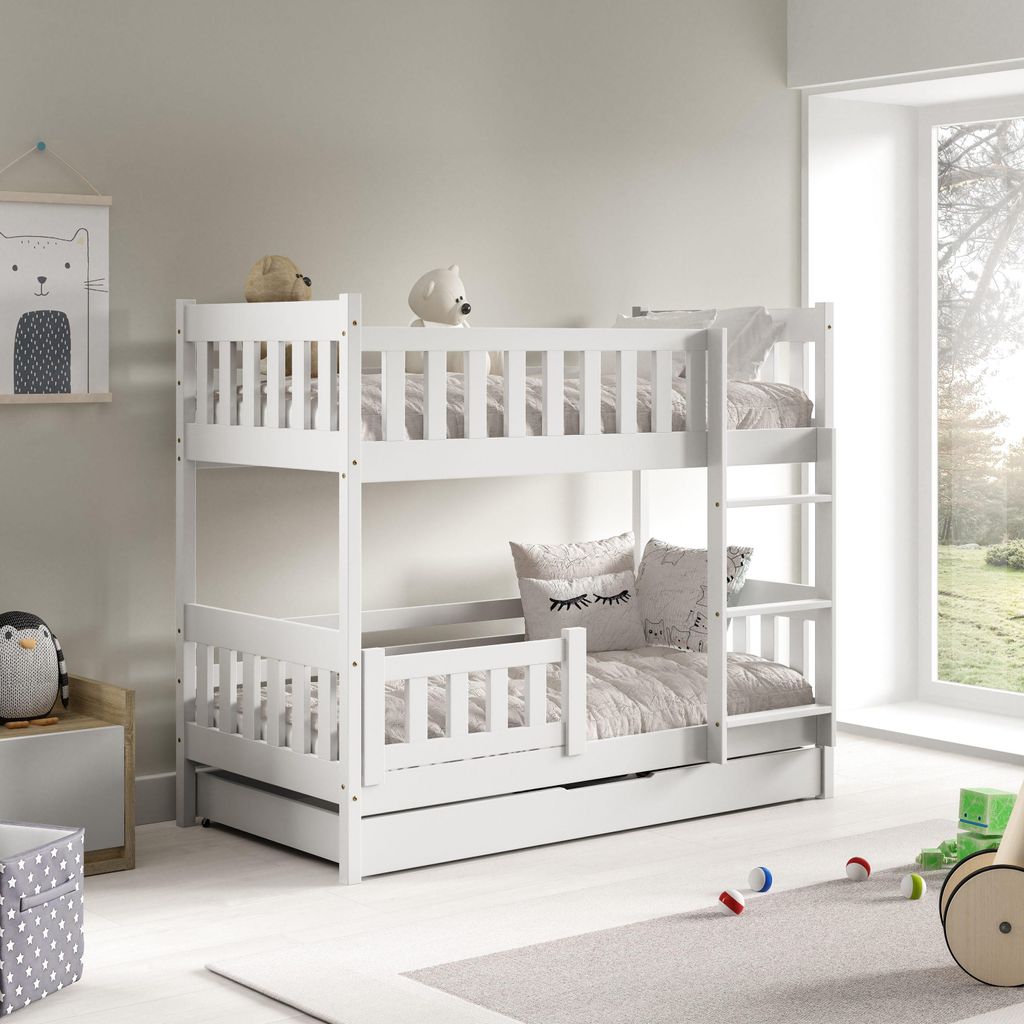 A white wooden bunk bed with a pull-out drawer, set up in a child's room with toys and a window view.