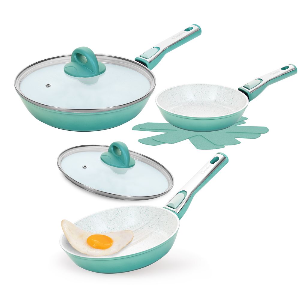 A set of teal and white ceramic frying pans with glass lids and a trivet, displayed on a white background. One pan contains a fried egg.