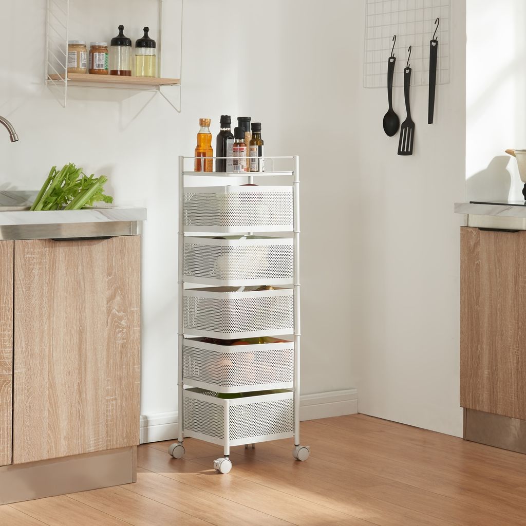 A kitchen scene with a white rolling cart filled with produce and bottles on top, next to a wooden cabinet and sink.