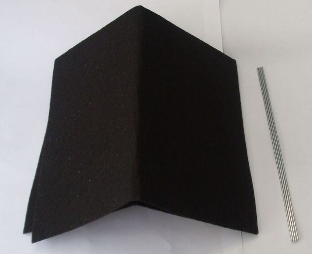 A black charcoal filter with a V-shaped crease and a few silver metal rods lying next to it on a white background.