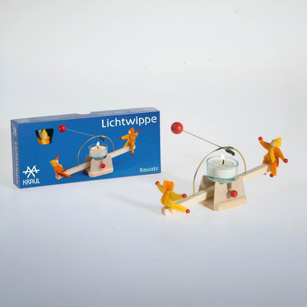 A wooden candle holder with figures on a seesaw, next to its packaging.