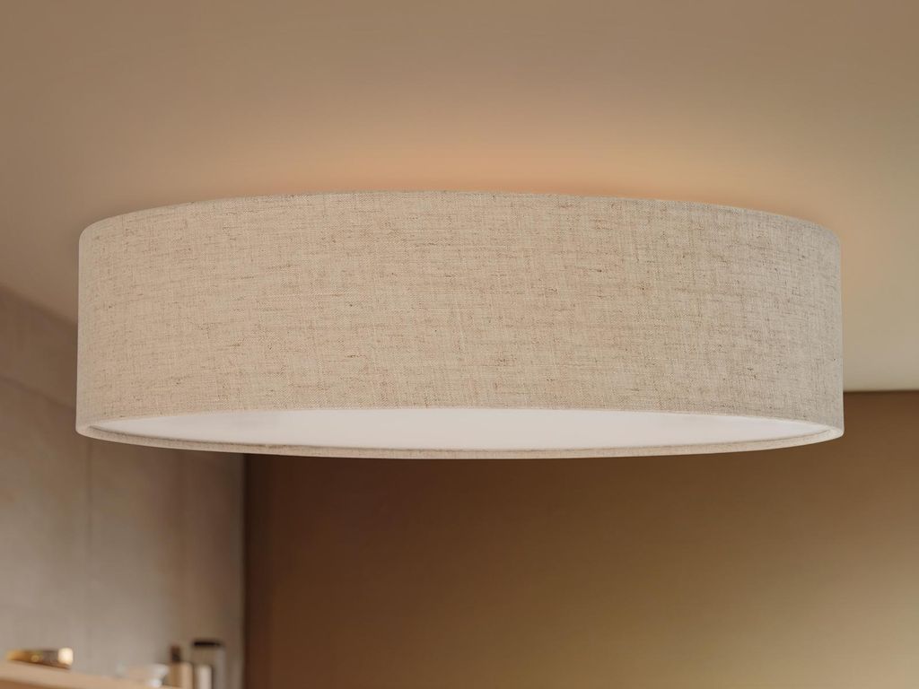 A close-up shot of a round LED ceiling light with a linen fabric shade, mounted on a beige ceiling.
