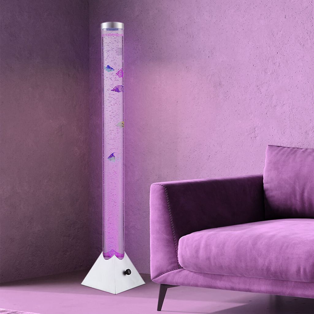 A tall, clear bubble lamp with purple water and decorative fish is placed next to a plush purple sofa in a room with purple walls.