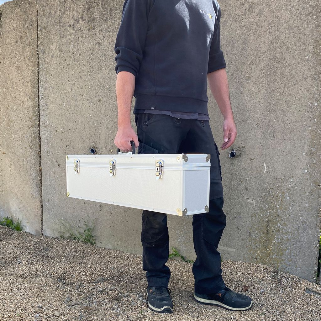 A person is holding a silver case in front of a concrete wall.
